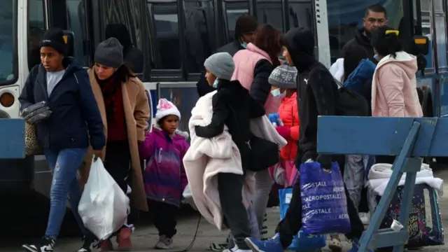 Dozens of migrants, carrying their belongings in bags, board local “warming buses” after being dropped off in Chicago in January 2024