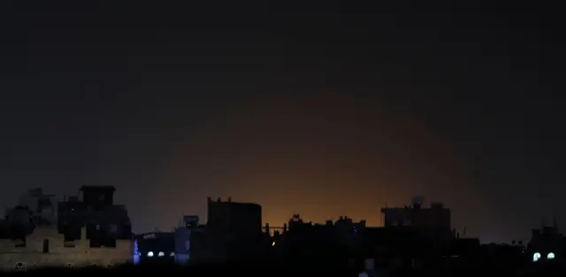 A general view of light shining behind buildings at a neighborhood following strikes in Yemen on 3 February.