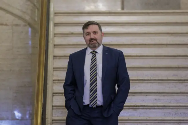 Robin Swann walks through the Great Hall at Stormont with hands in pockets