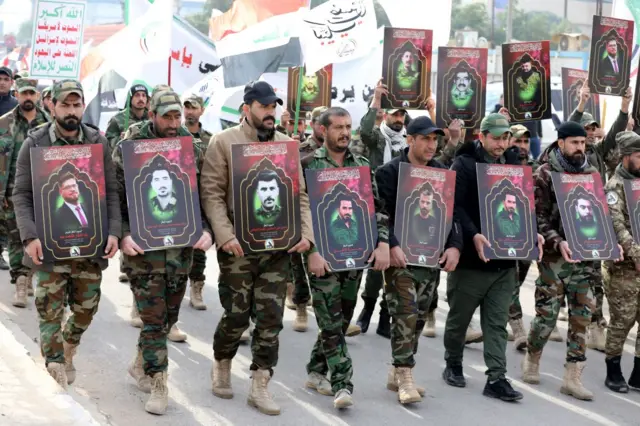 Militia men carry images of comrades killed in US air strikes during funeral procession in Baghdad