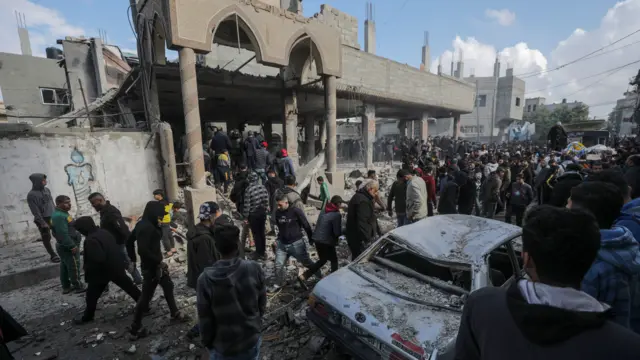 Palestinians search through the rubble of a destroyed mosque in Deir al-Balah, with a destroyed car visible in the foreground