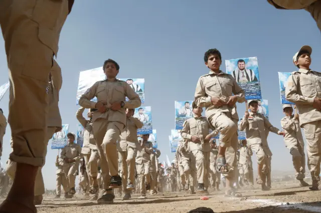 A scout team of boys carrying placards of the Houthi leader and marching in step