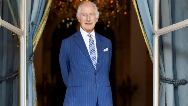 King Charles wears a blue suit with his hands behind his back