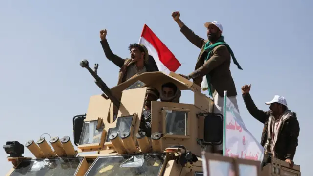 A number of men aligned with the Houthi movement pump their fists while riding on an armoured vehicle