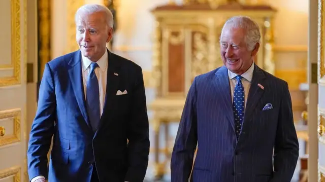 Biden and the King walk down an ornate hallway, laughing.