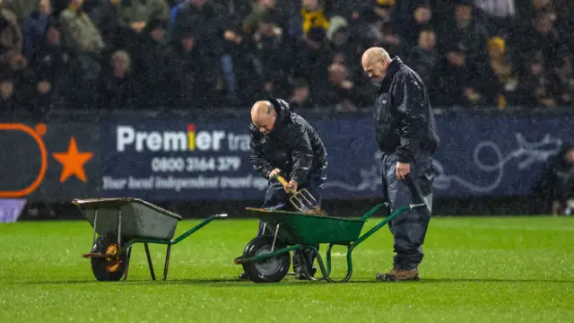 Groundsmen with wheelbarrows on pitch