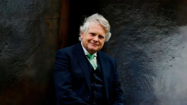 Lord Michael Dobbs sitting in front of a dark wall