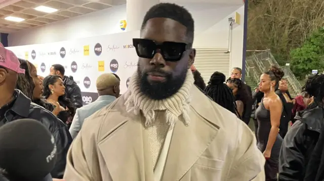 Rapper Ghetts wearing a white jumper and coat at the Mobos