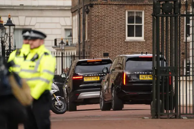 Two black SUVs are seen through the gate at Clarence House, as blurred policemen stand in the foreground on the left