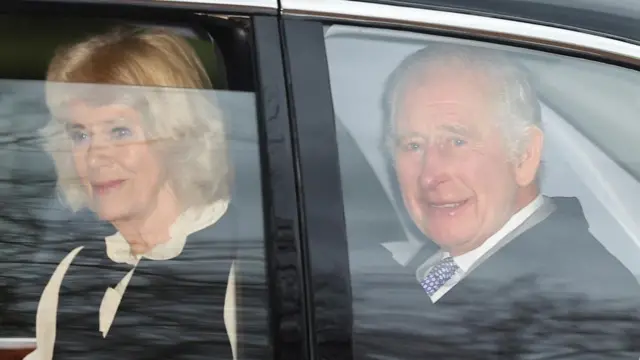 King Charles and Queen Camilla ride in the back seat of a car