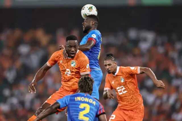 Mbemba reaches the ball above a crowded penalty area.