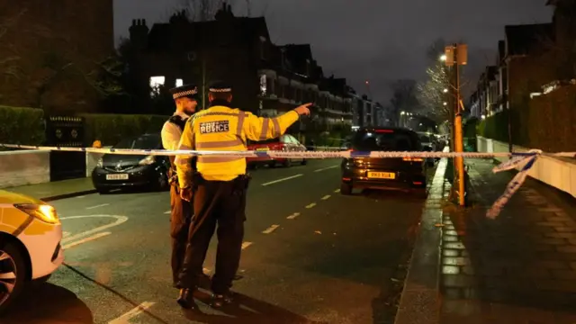 Two police speak on the other side of police tape sectioning off a residential road