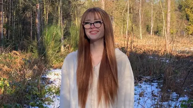 Brianna standing in a wooded area, covered in some snow, smiling