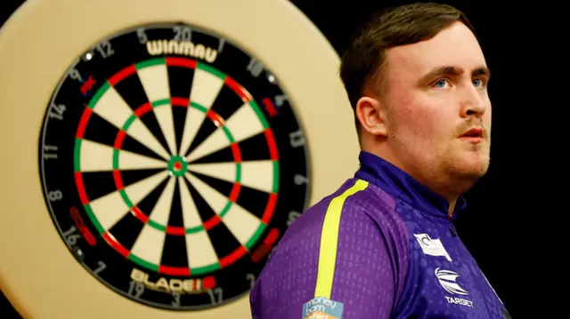 Luke Littler stands in front of a dartboard