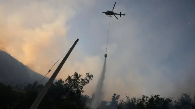 A helicopter makes a water drop as a wildfire burns parts of the rural areas of Santiago, Chile