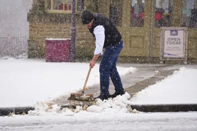 A person clears snow in front of the Opera House in Buxton