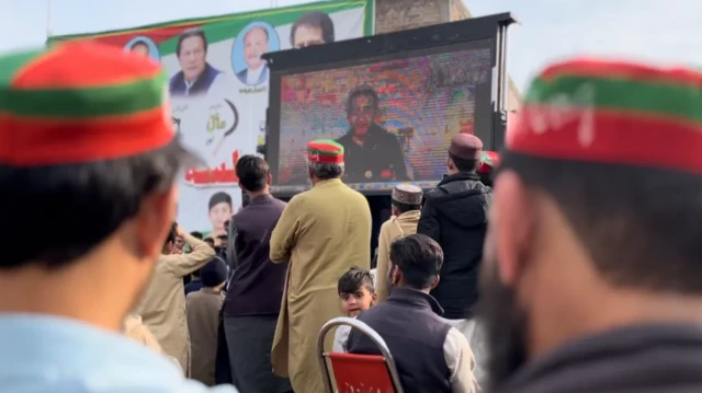 PTI supporters attend a rally where the main speaker is on a screen