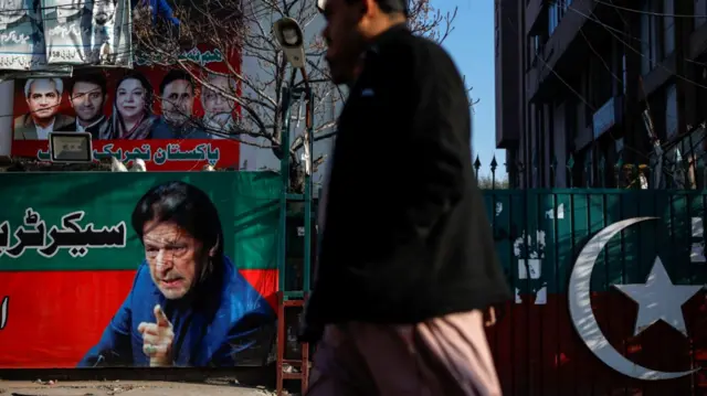 People walk past a banner with a picture of the former Prime Minister Imran Khan outside the party office of Pakistan Tehreek-e-Insaf (PTI), a day after the general election, in Lahore, Pakistan, February 9, 2024