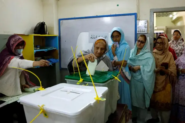 A polling officer instructs a woman, as she casts her vote at a polling station during the general election in Karachi, Pakistan February 8