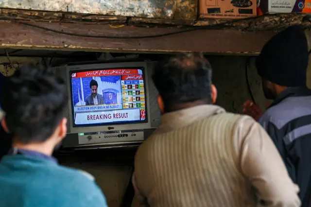 People monitor latest election results live on a television at a tea shop in Lahore