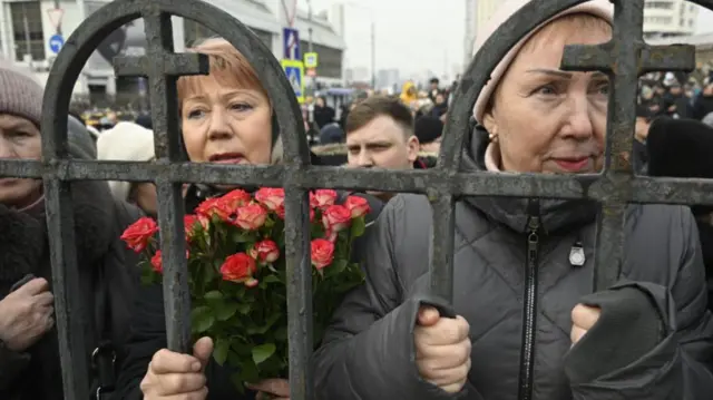 Mourners stand by the railings near the chruch