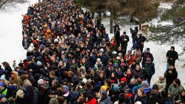 A crowd of people, some holding roses, walk towards the Borisovskoye cemetery where Alexei Navalny was buried