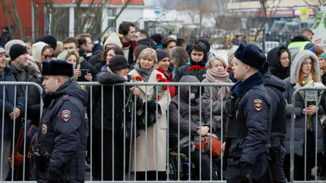 Police officers walk past people, who gather outside the church