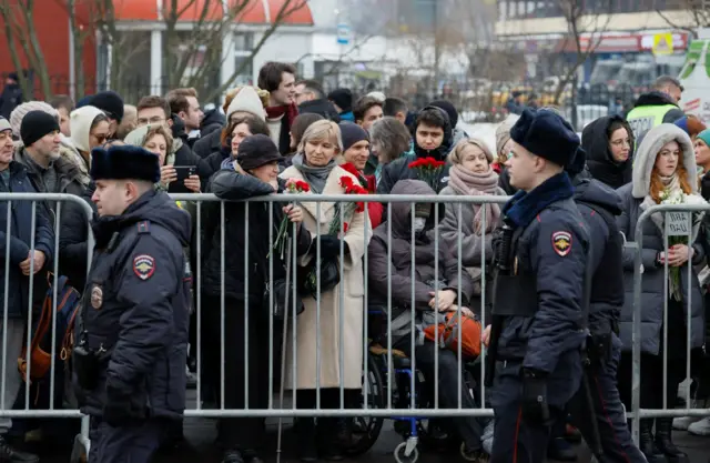 Police officers on guard as people stand behind metal barriers erected near the church in Moscow where Alexei Navalny's funeral is expected to take place