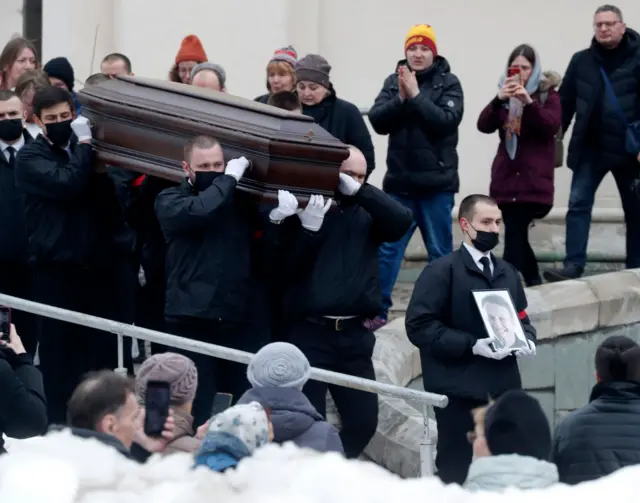 Funeral service workers carry out Alexei Navalny's coffin after his church funeral service