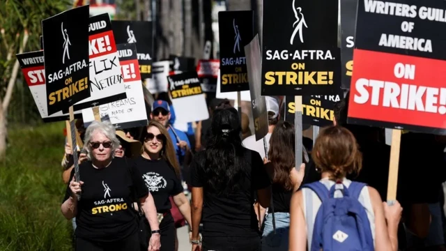 Actors, writers and crew members march outside a Hollywood studio, holding strike placards