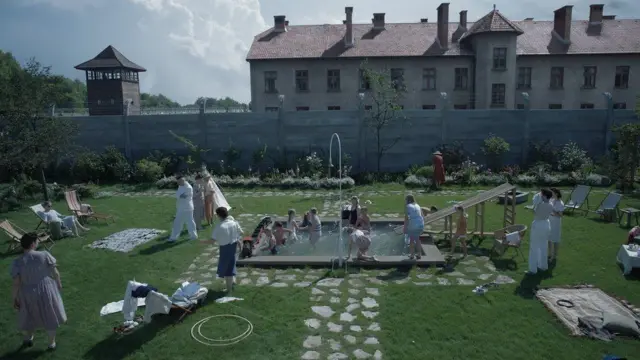 A family enjoys a swimming pool in a backyard sharing a fence with Auschwitz