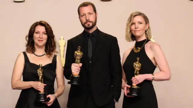 Raney Aronson-Rath, Mstyslav Chernov, and Michelle Mizner hold their Oscars, not smiling.