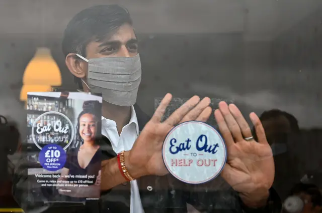 The then Chancellor of the Exchequer Rishi Sunak places an Eat Out to Help Out sticker in the window of a business