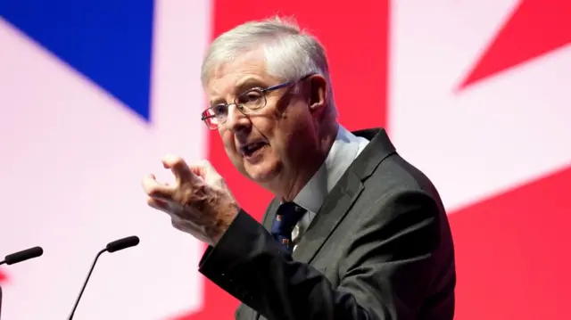 Mark Drakeford speaks at a lectern in front of a projection of the Union Jack flag