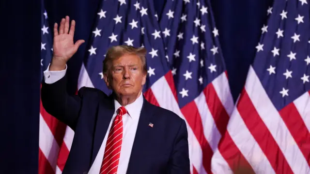 Donald Trump waves in front of US flags