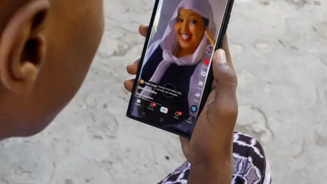 Abdulahi Ahmed uses his mobile phone to watch a video on social media app TikTok, outside their home in Waberi district of Mogadishu, Somalia August 21, 202