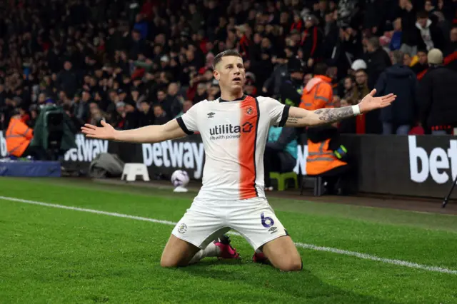 Ross Barkley slides on his knees and holds his arms out wide to celebrate his goal.