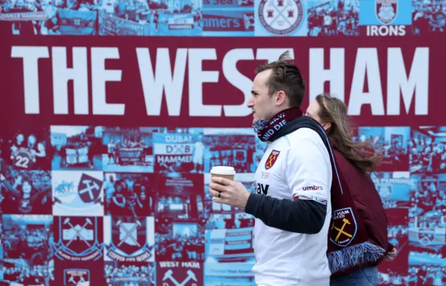 West Ham fans carry coffees as they walk around the ground in club colours.