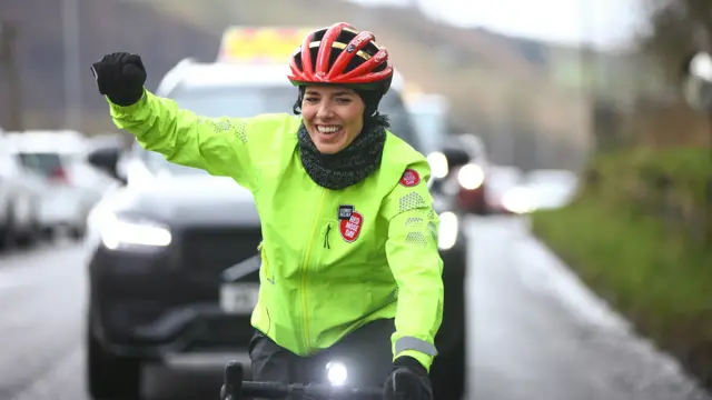 Mollie cycles with her arm raised in a 'fist pump'