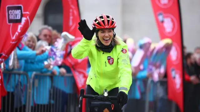 Mollie cycles through the finish line smiling and waving