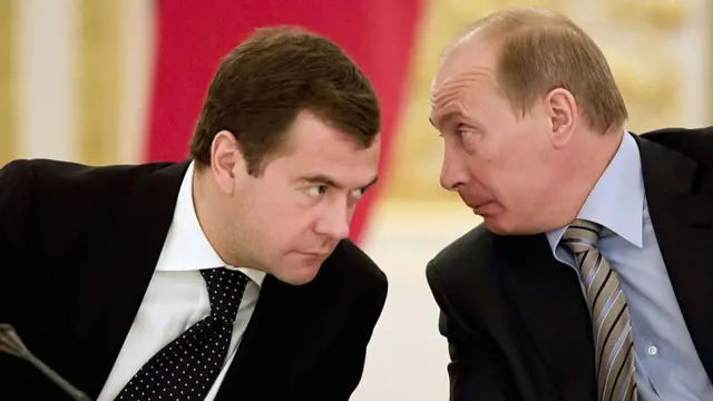 Putin speaks into the ear of Medvedev