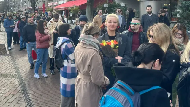 Navalnaya is holding flowers while standing in the line with the people in front of a polling station in Berlin