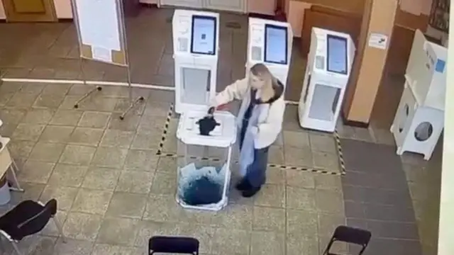 A woman pours a liquid into a ballot box, during the Russian presidential election in Moscow, Russia, in this screen grab taken from a video recording of a screen showing CCTV footage, March 15, 2024.