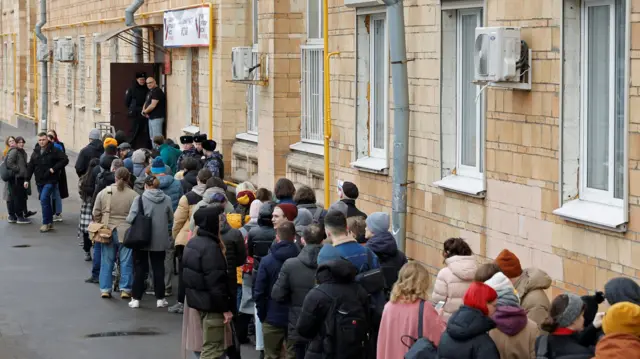 People stand in a line to enter a polling station around noon on the final day of the presidential election in Moscow, Russia