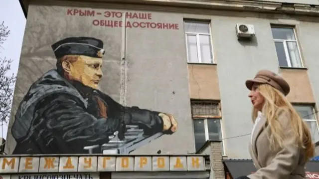 A woman walks past a mural of Russian President Vladimir Putin in Simferopol in Crimea, 12 March 2024