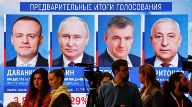 People gather near a screen showing the preliminary results of Russia's presidential election