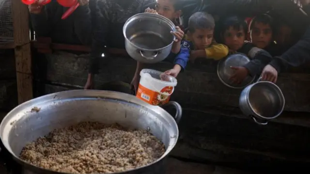 Children in Rafah, Gaza  wait to receive food cooked by a charity kitchen amid shortages of food supplies