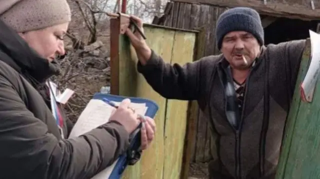 A woman with a clipboard gives a man in occupied Ukraine voting papers