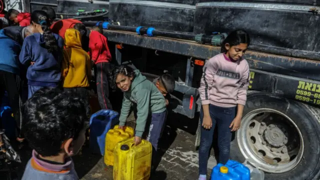 Two young girls stand with dirty jerry cans next to the tires of a truck