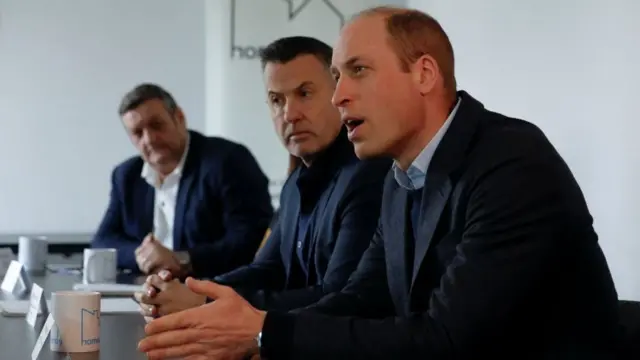 William is pictured mid-sentence sitting at a black table alongside two men